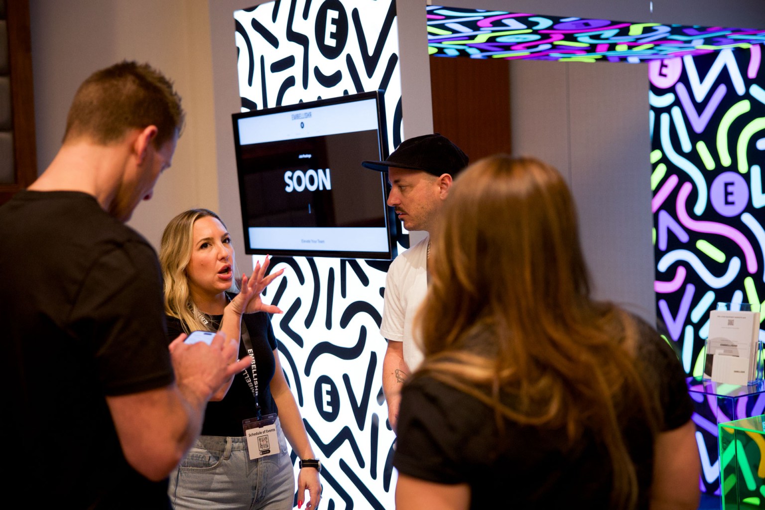 Nicole Pape and her team at Embellishr chat with Ryan Moor and Jenna Sackett on the show floor. At Embellishr, you can shop or sell used screen printing and embroidery equipment.